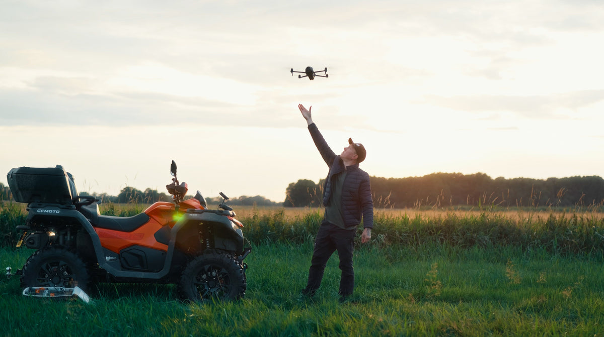 Tom Przibilla neben seinem Quad auf einer Wiese, mit einer Drohne über seiner ausgestreckten Hand