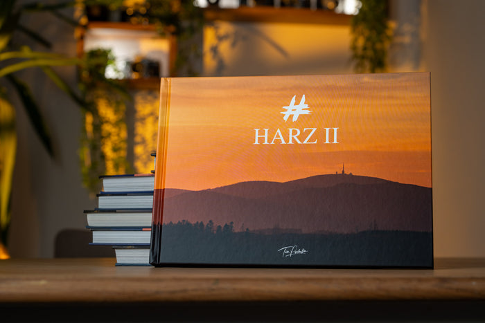 HARZ II Bildband von Tom Przibilla, aufgestellt neben einem Bücherstapel: orangefarbenes Cover mit Brocken-Silhouette.