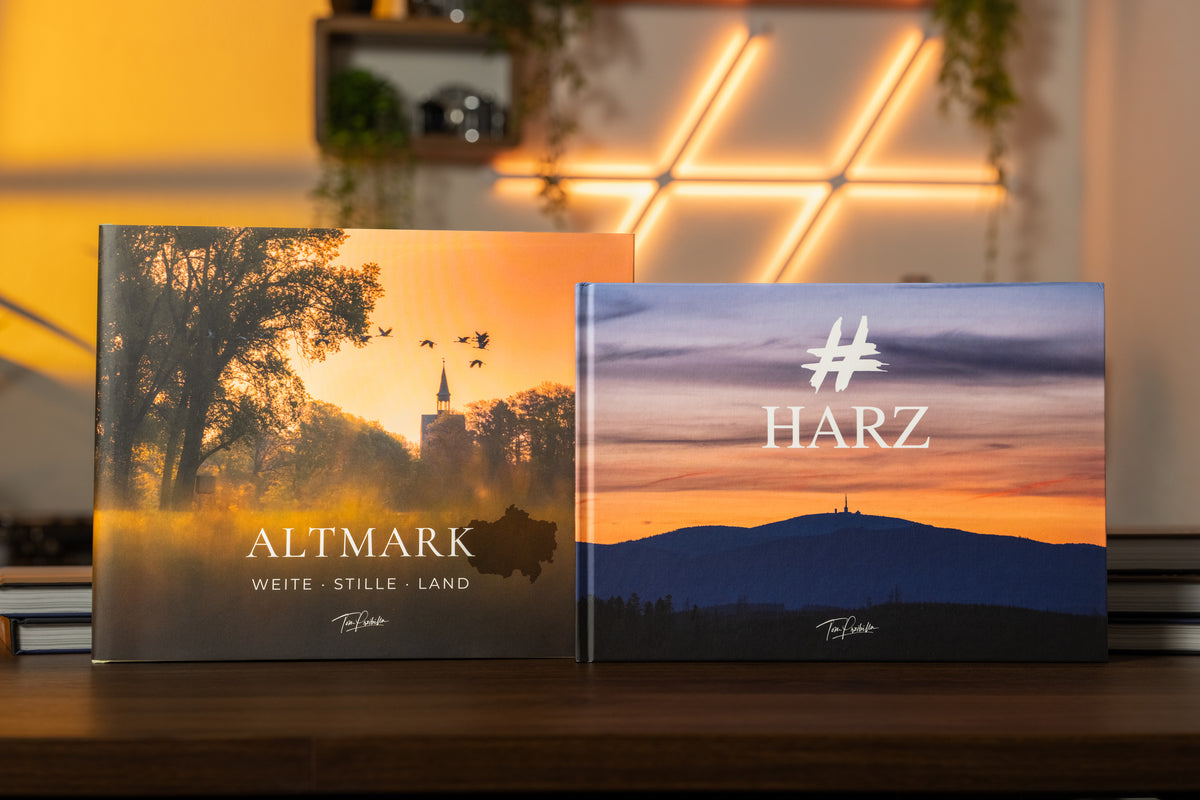 ALTMARK und HARZ als Bildband-Set: Beide Bücher mit ihren Landschaftscovern nebeneinander auf einem Holztisch im warmen Abendlicht.