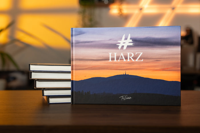 HARZ Bildband von Tom Przibilla: Hardcover mit Brocken-Silhouette im Abendlicht, aufgestellt auf einem Holztisch neben einem Bücherstapel.